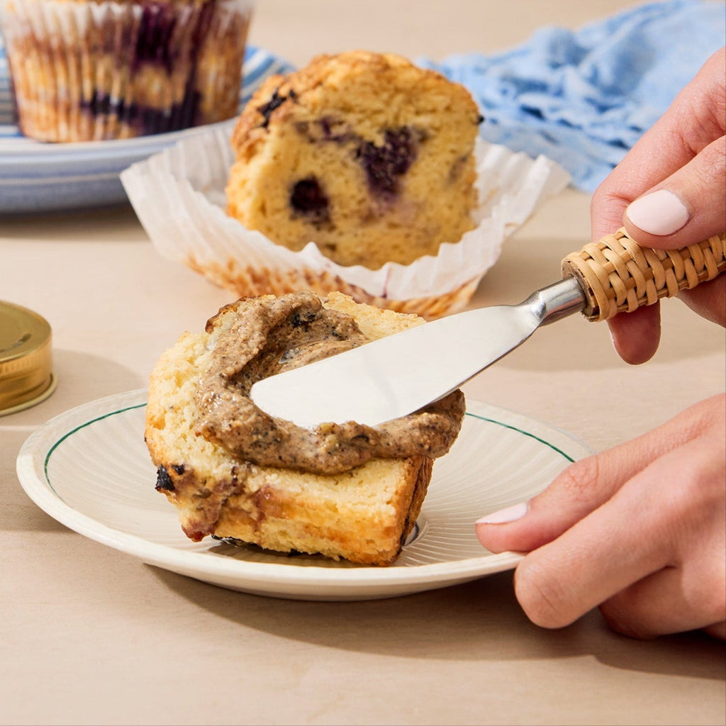 Person spreading blueberry muffin nut butter on a bakery-style blueberry muffin.